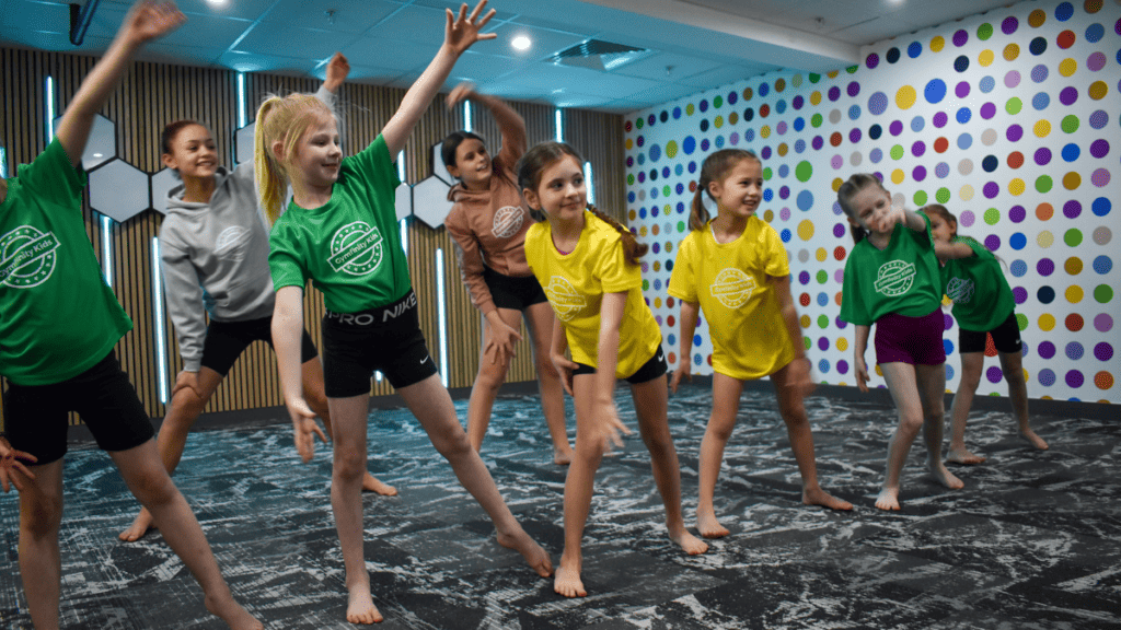 Children doing gymnastic exercise indoors, kids in colorful sportswear participating in a fitness activity, fun, energetic, and inclusive environment in a modern gym or sports centre, smiling and engaging in physical activity, learning teamwork and fitness.