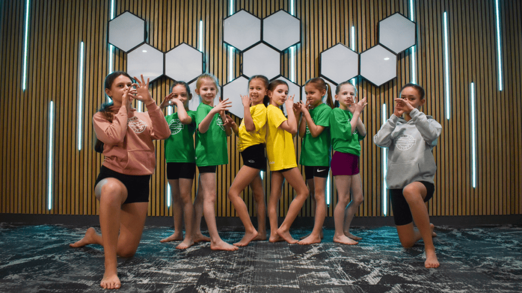 Children doing gymnastic exercise indoors, kids in colorful sportswear participating in a fitness activity, fun, energetic, and inclusive environment in a modern gym or sports centre, smiling and engaging in physical activity, learning teamwork and fitness.