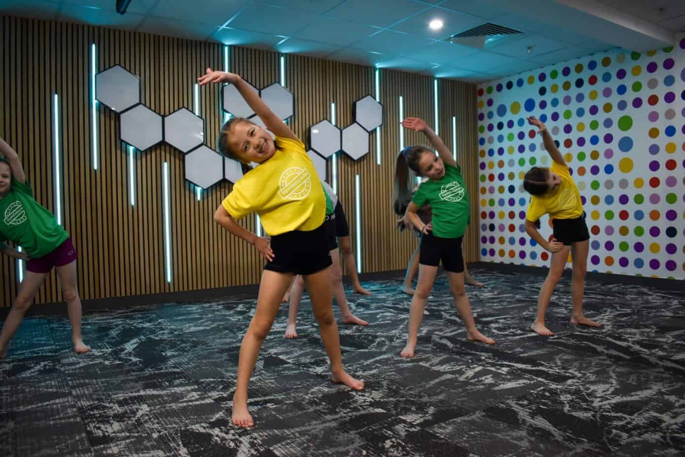 Bright young girls in colourful t-shirts perform a dance routine in a modern indoor studio with artistic wall decor and colourful polka dots.