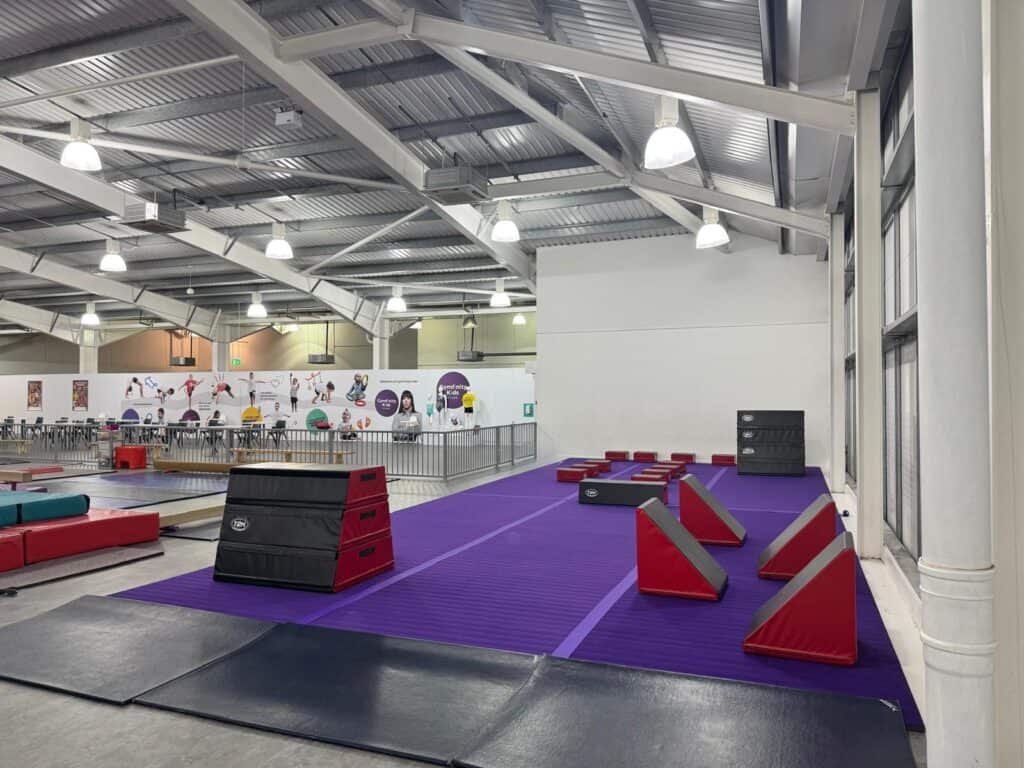 Indoor skatepark with ramps, rails, and foam pits for skateboarding, BMX, and scooter tricks in a spacious, well-lit facility with high ceilings and modern design.