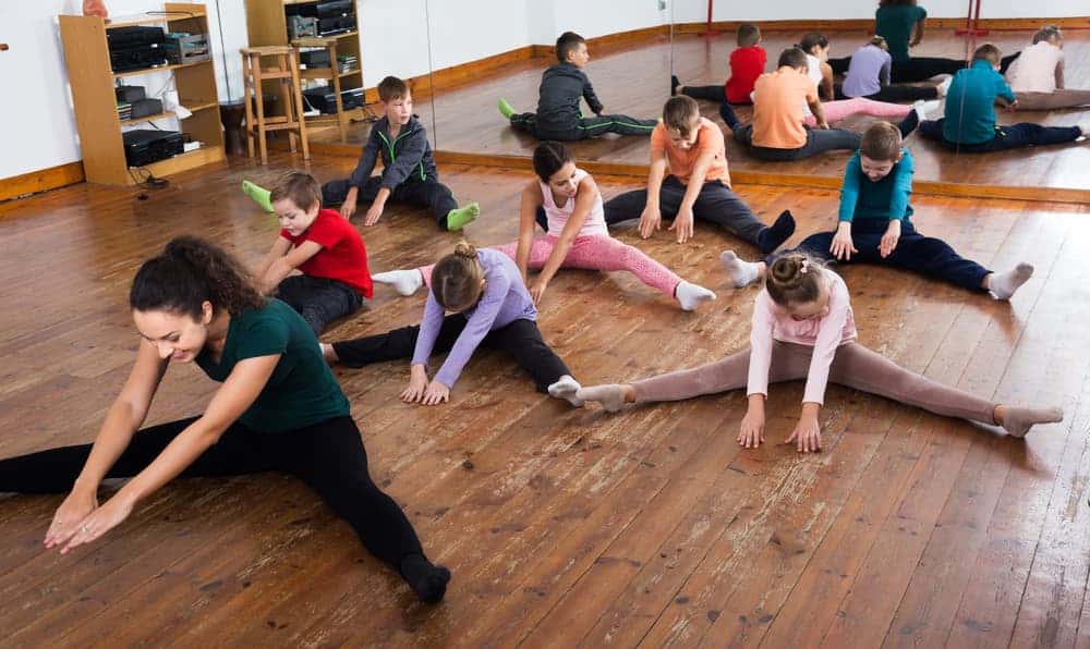 Flexible children stretching on wooden floor in dance or gymnastics class indoors.