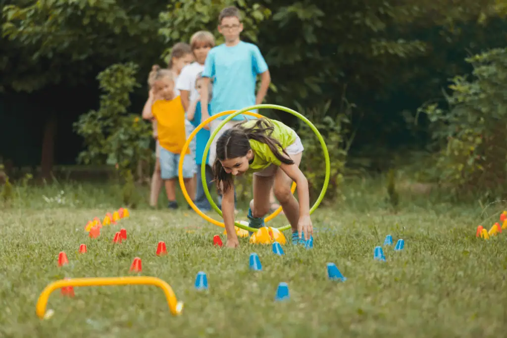 Children participating in a backyard obstacle course game outdoors with friends on a sunny day.