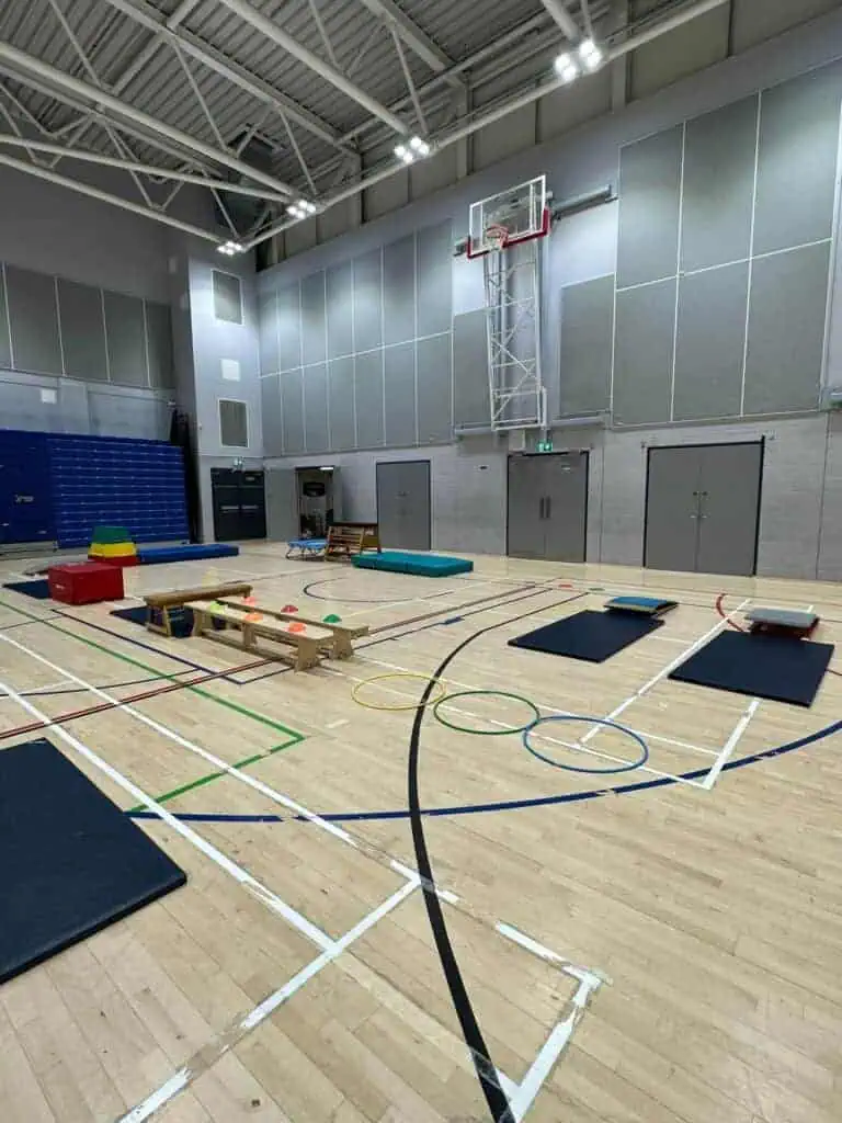 Hall with gym equipment and sports mats set up for physical education activities in a spacious indoor sports hall.