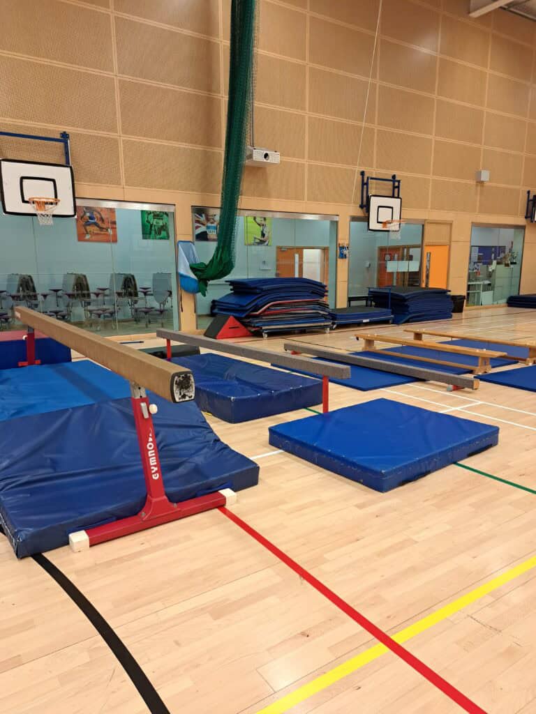 An indoor gymnasium with gymnastics mats, vaulting equipment, and basketball hoops on the walls, ready for training or competitions.