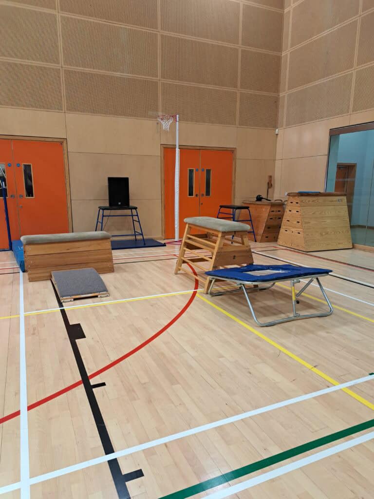A colourful indoor gymnasium with various exercise equipment including a trampoline, balance beams, and mats, designed for physical therapy or fitness activities.