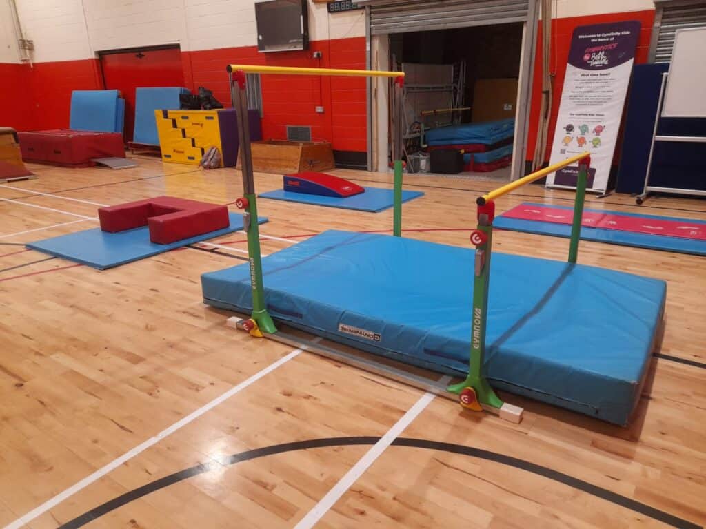 Climbing and gymnastics equipment set up inside a gymnasium for children's activities, including mats, bars, and soft blocks for safe play and exercise.