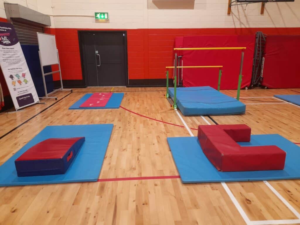 Colourful indoor gymnasium setup with soft mats, balance beams, and gymnastic climbing equipment for children’s physical activity and play.