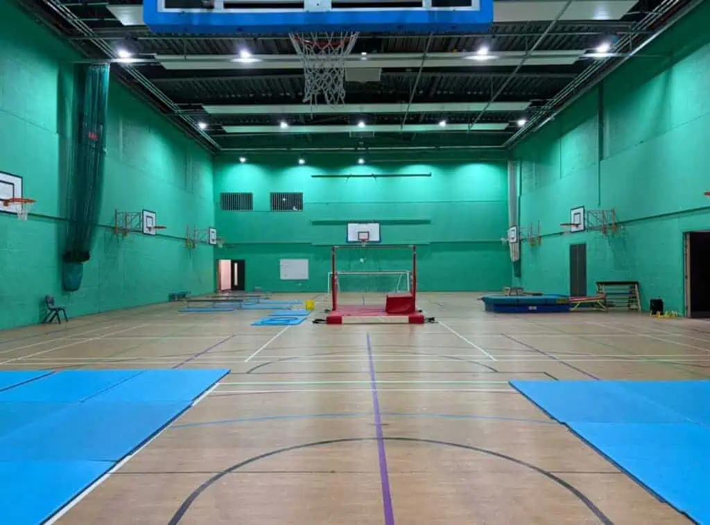 Indoor sports hall with basketball hoops, padded mats, and training equipment on a wooden court, suitable for basketball, volleyball, and fitness activities.