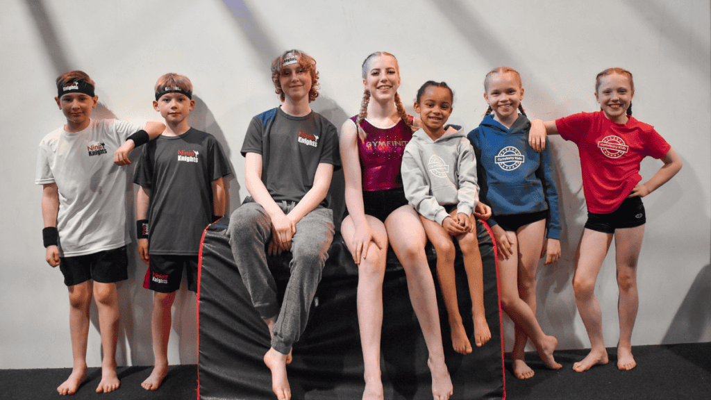 Kids martial arts class with children in sportswear, smiling and sitting on foam blocks after training, in a gym with plain wall background.