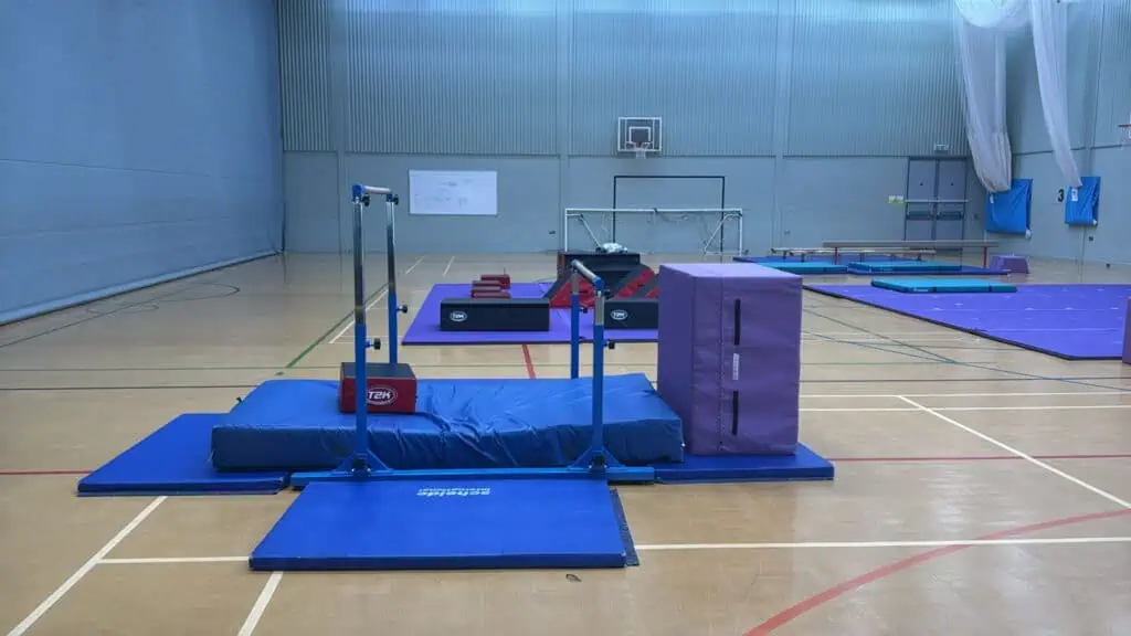 Padded gymnastics training area with mats, bars, and a trampoline inside a sports hall. Suitable for gymnastics practice and training sessions.