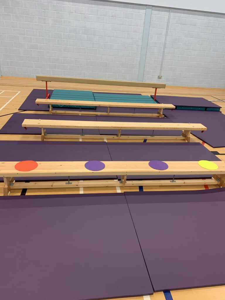 Benches and foam mats arranged on a wooden gym floor for a sporting event or physical activity.