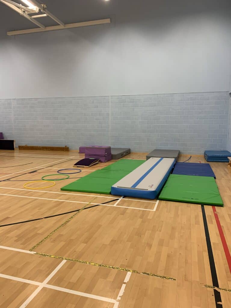 Jumping and balance training equipment set up on a wooden gym floor; includes mats, hoops, and various padded gear for fitness exercises and physical therapy.