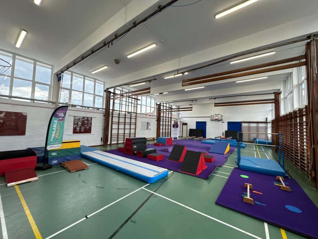 Children's indoor soft play gym with various climbing and balancing equipment in a spacious sports hall alt text.