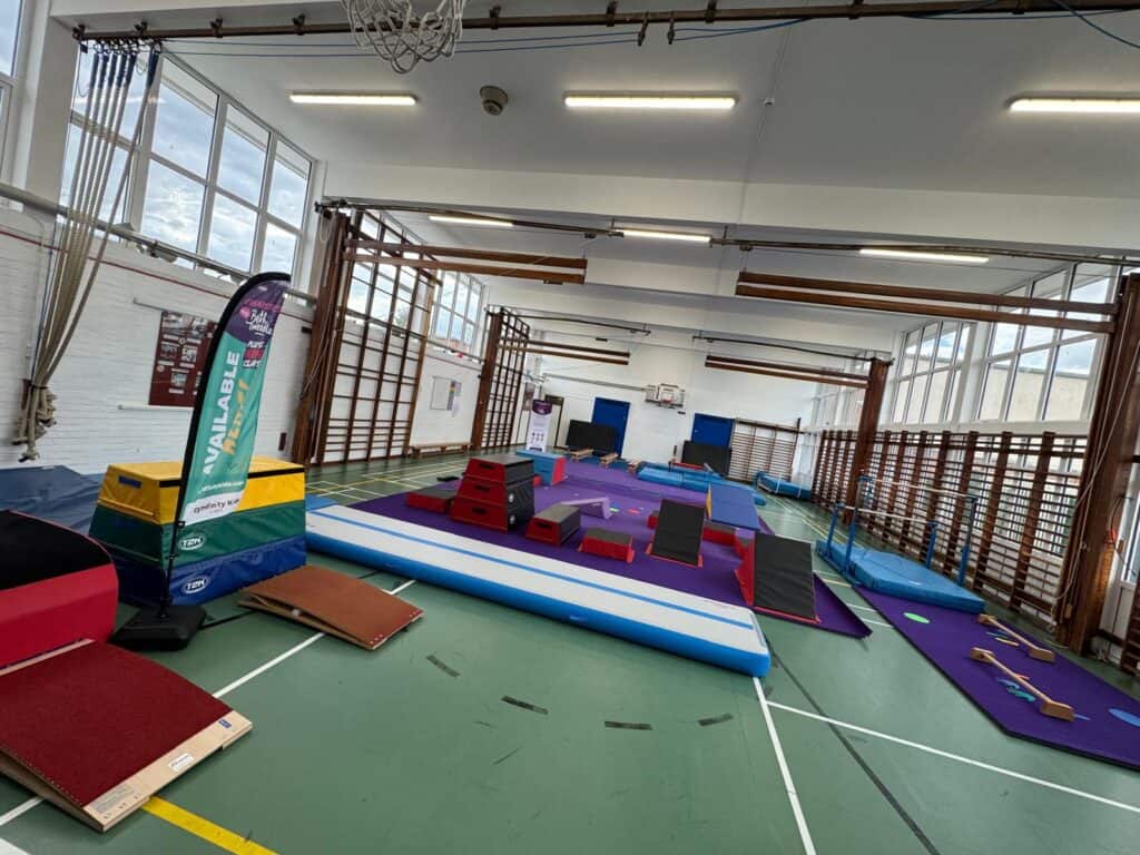 Bright indoor gymnasium set up for gymnastics or trampoline training, featuring foam pits, mats, and training equipment, with large windows allowing natural light, ideal for gymnastics practice.