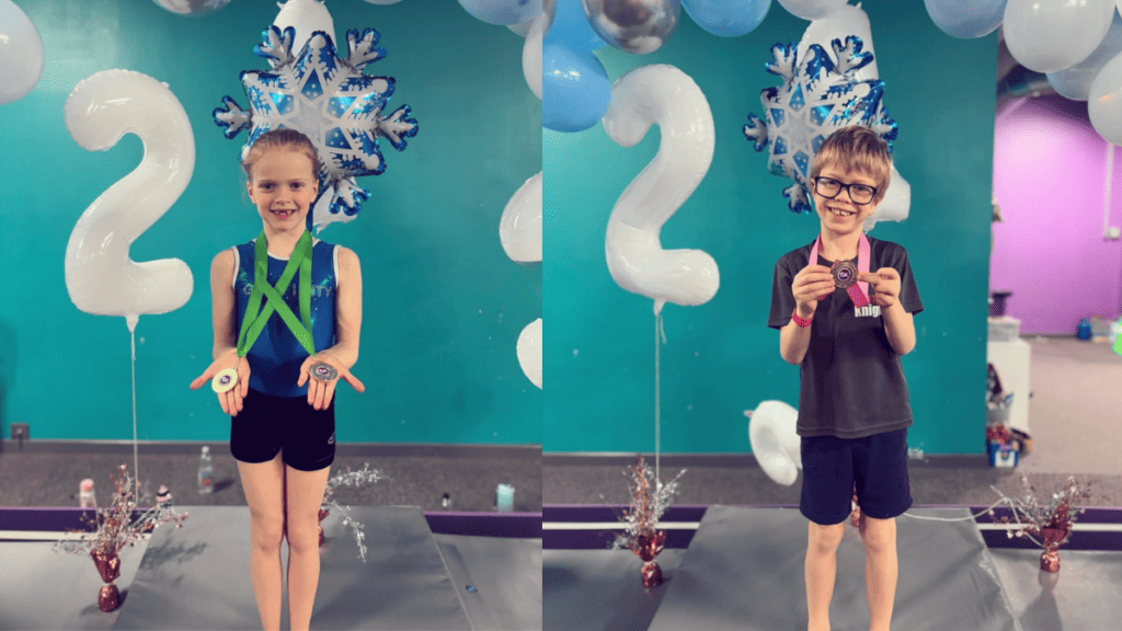 Medal-winning girl and boy at a skating competition, celebrating their achievements with medals, standing in front of a colourful winter-themed backdrop with balloons and number '2' balloons.