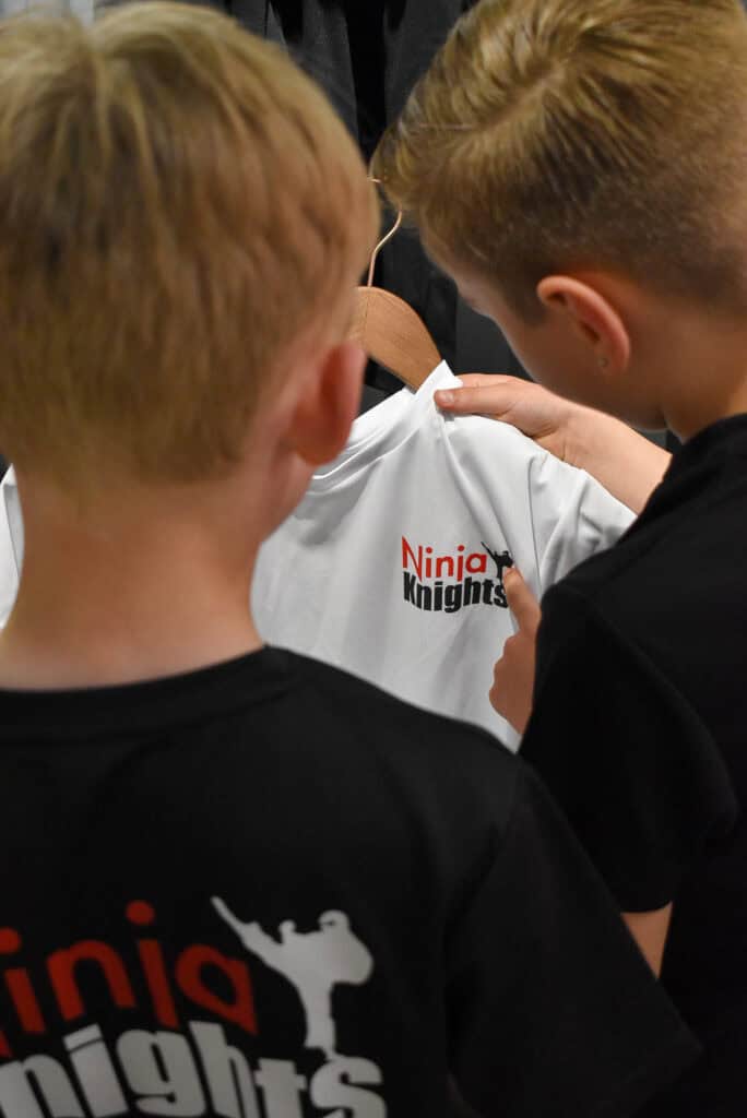 Helmet with Ninja Knights logo being inspected by two young boys wearing Ninja Knights t-shirts.