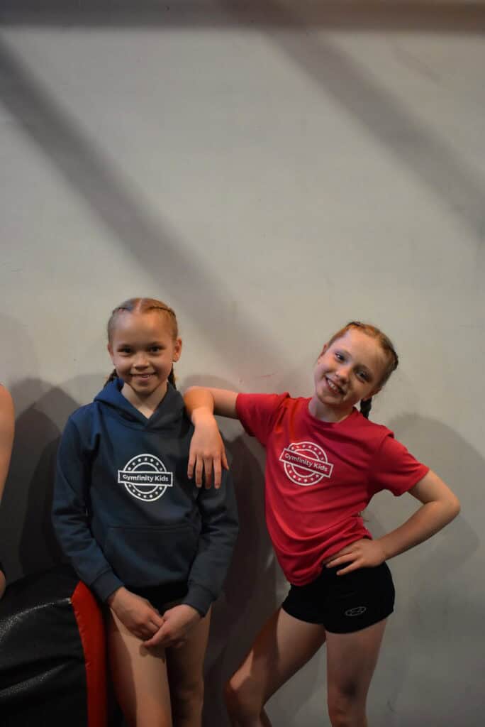 Smiling young girls in Gymfinity Kids sportswear posing together indoors.