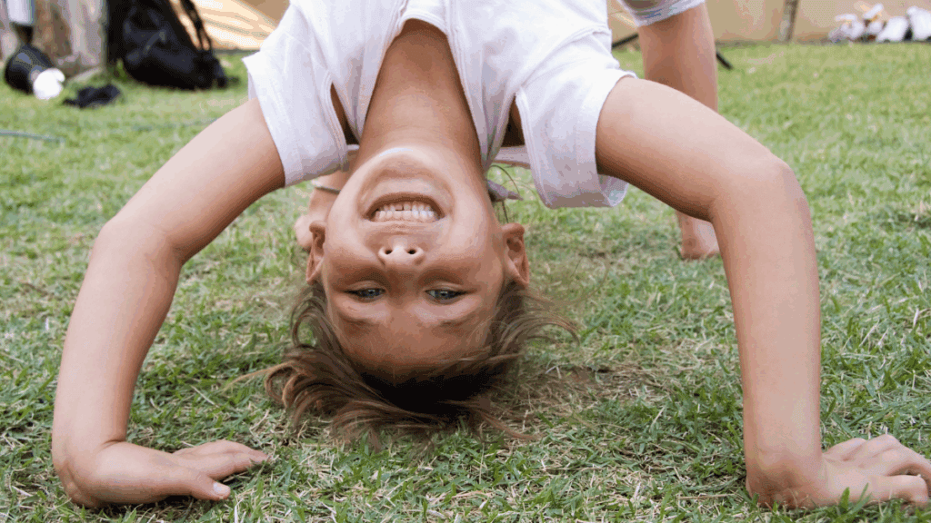 Handstand girl doing a headstand on the grass in a backyard garden.