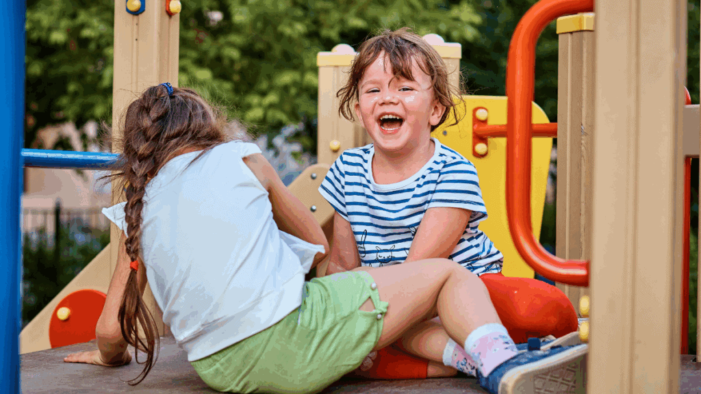 Childhood friends laughing and playing on colourful playground equipment in a park. Joyful outdoor activity, summer day, childhood happiness, kids having fun.