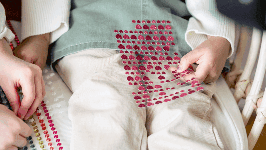 Rainbow coloured rhinestones being applied to clothing by a person’s hand.