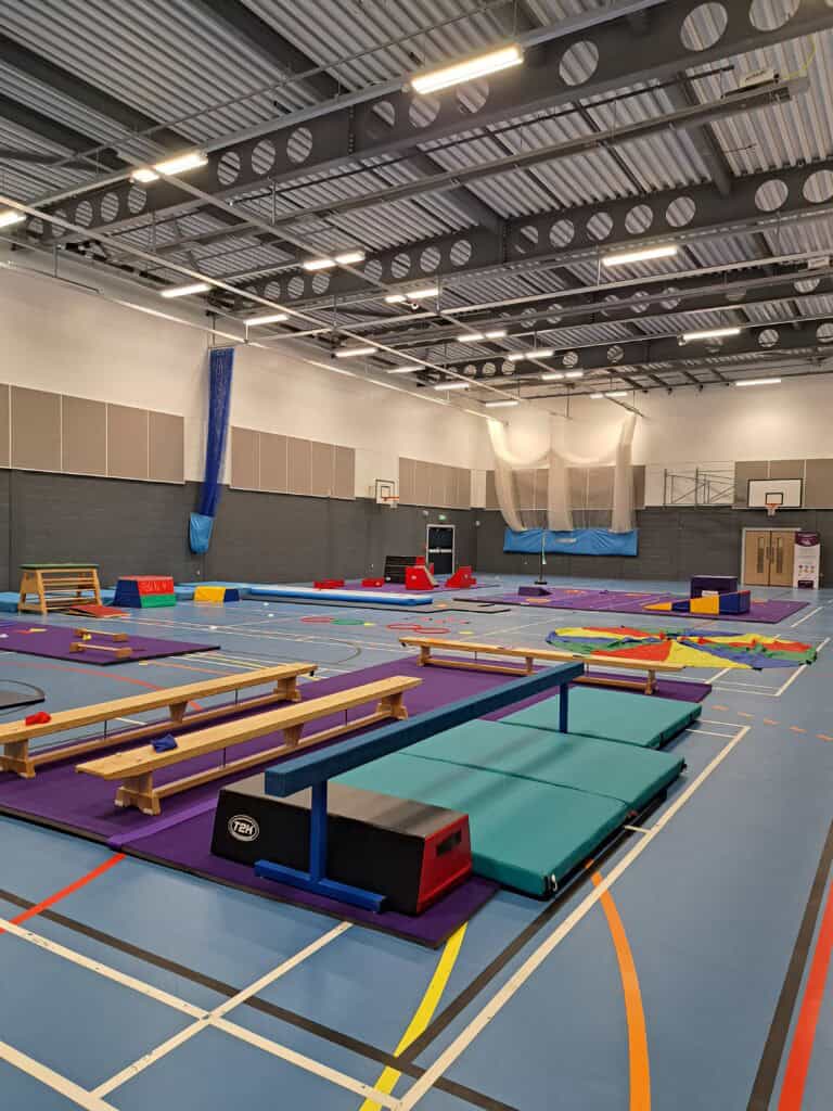 Climbing gym indoor training area with mats, balance beams, and gymnastic equipment inside a spacious sports hall.