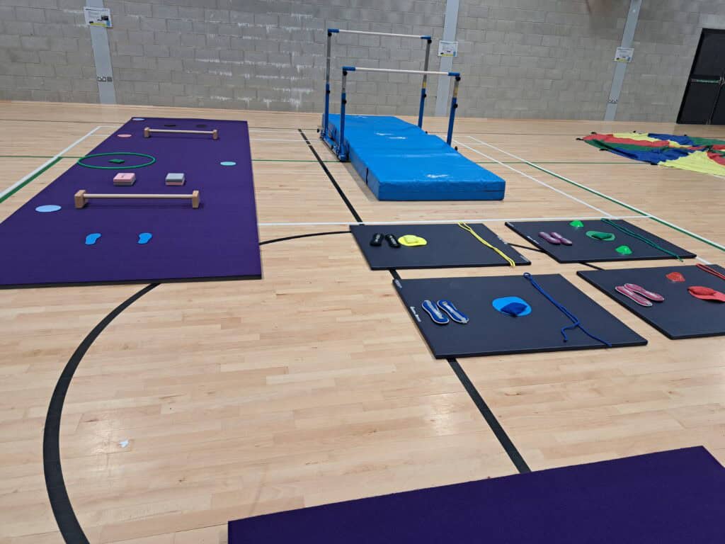 Gymnastics training setup with mats, vault, and various equipment in an indoor sports hall.