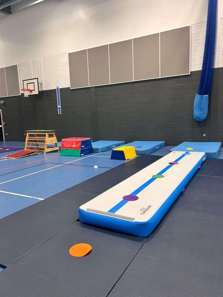 Multisport gymnasium with gymnastics mats, vaulting boxes, and agility equipment set up for children or athletes training in a spacious indoor sports facility.