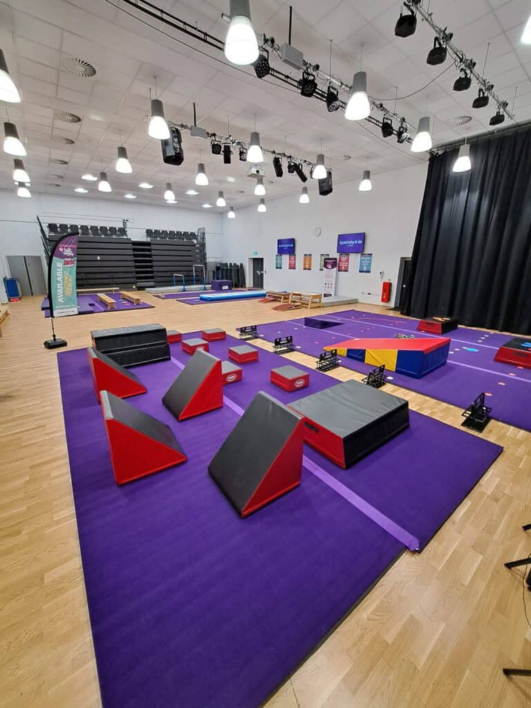 A detailed indoor gymnasium setup with various fitness equipment, mats, and obstacle courses designed for physical training and activities.