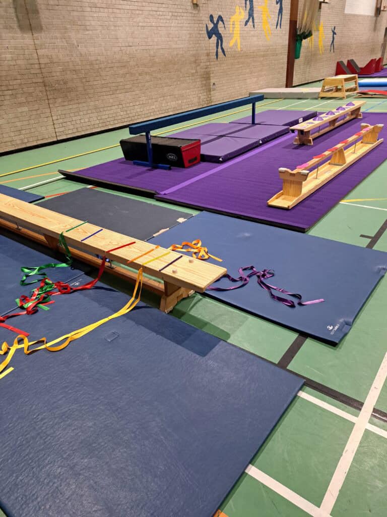 Indoor gymnastics training area with mats, vaulting equipment, and benches in a gymnasium setting.