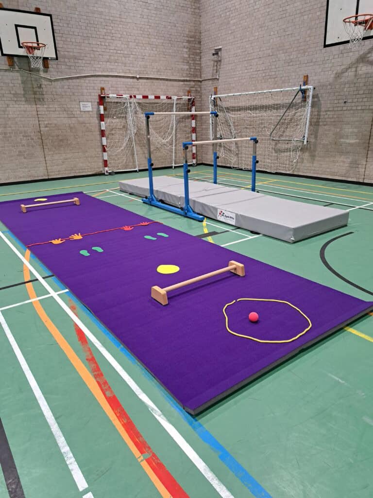Jumping and agility training setup in an indoor sports hall with gymnastic mats, hurdles, and cones for physical exercises and sports practice.