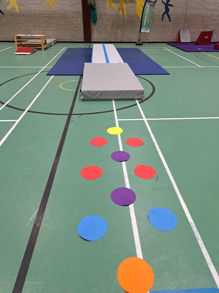 Jumping and landing mats set up in a gymnasium for physical activities and training exercises. The mats are placed on a sports hall floor with various coloured cones and equipment around.