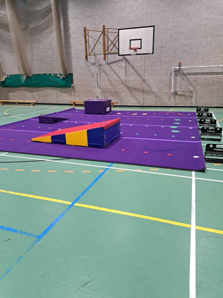 An indoor sports hall with gymnastic mats, vaulting equipment, and basketball hoops, suitable for gymnastics, basketball, and other indoor sports activities.