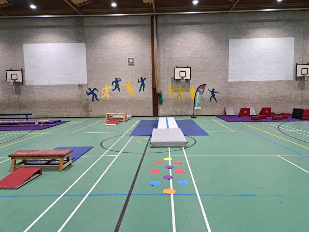 Jumping and agility training setup in an indoor sports hall with gymnastic mats, hurdles, and colorful cones for children or athletes.