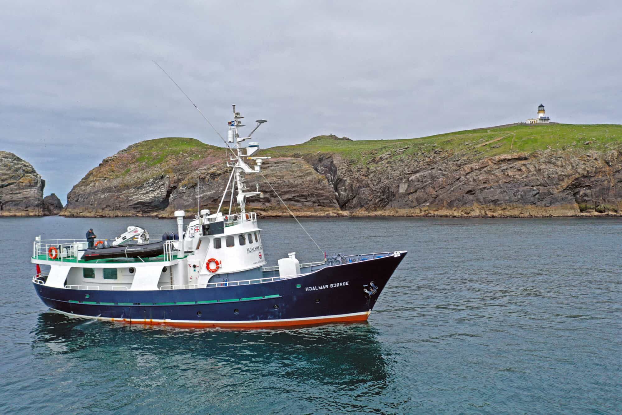 Scenic boat cruising in the Hebrides with rugged coastline and lighthouse views.