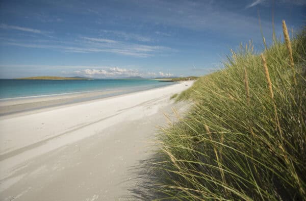 Scenic Hebridean beachscape with white sands, dunes, and turquoise waters under blue skies.