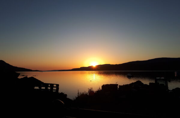 Stunning sunset over the Hebrides, featuring tranquil waters, boats, and mountain silhouettes, perfect for exploring Scottish islands.