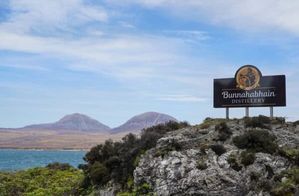 Scenic view of Bunnahabhain Distillery on Skye with mountains and sea in the background, ideal for whisky lovers exploring Hebridean distilleries.