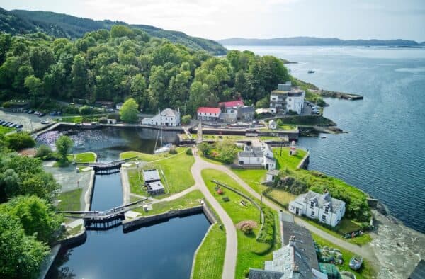 Aerial view of Hebridean harbour and seaside village, showcasing lush green landscapes and tranquil waters.