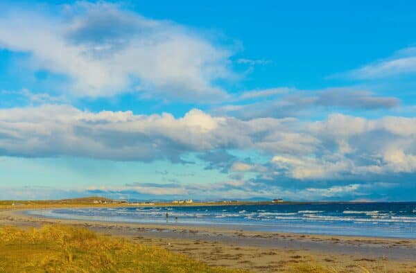Vast sandy beach under blue sky with clouds, overlooking Hebridean islands, perfect for relaxing walks.
