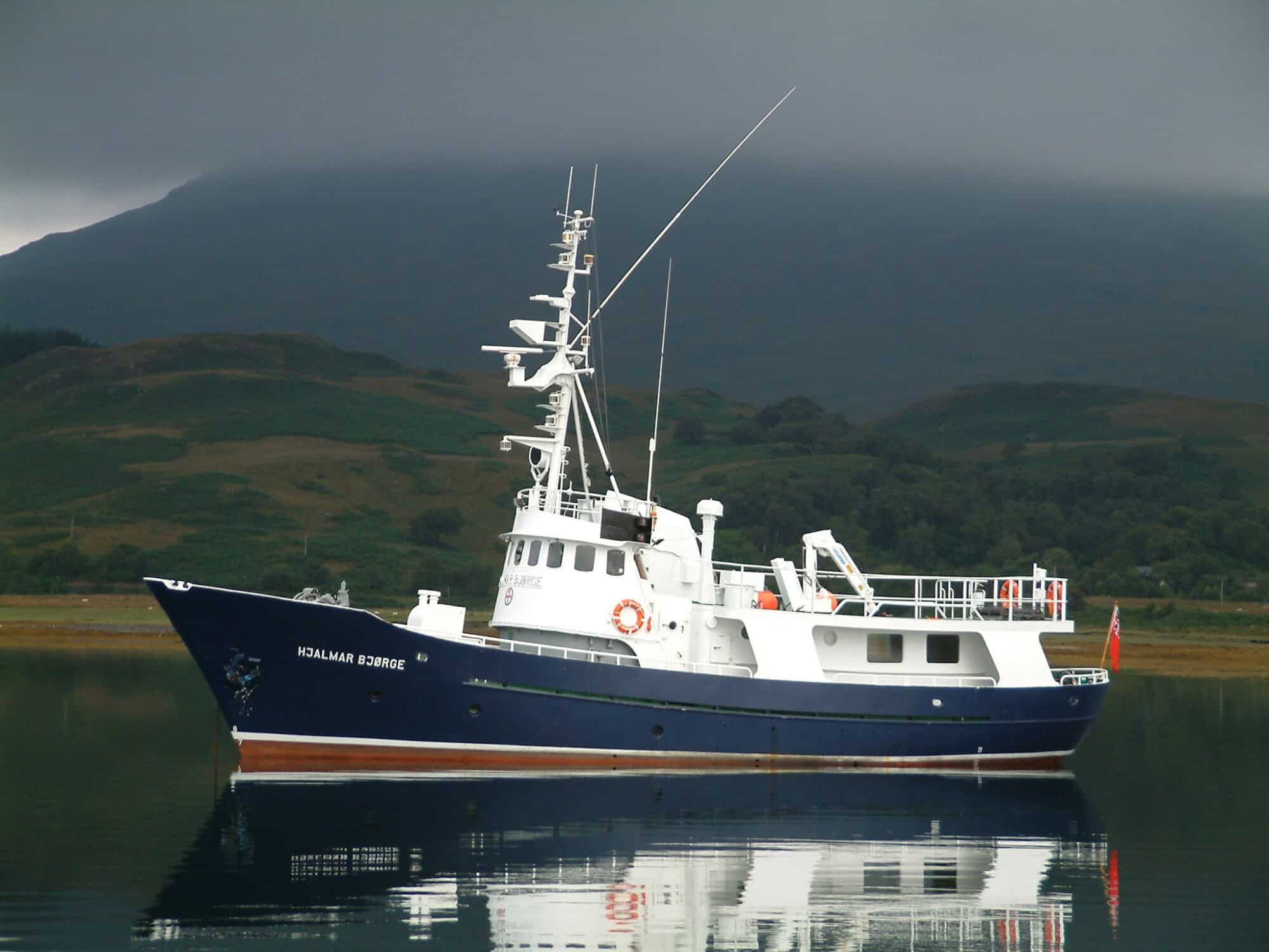 Vessel on calm waters with dramatic mountain backdrop, ideal for coastal exploration and wildlife spotting.