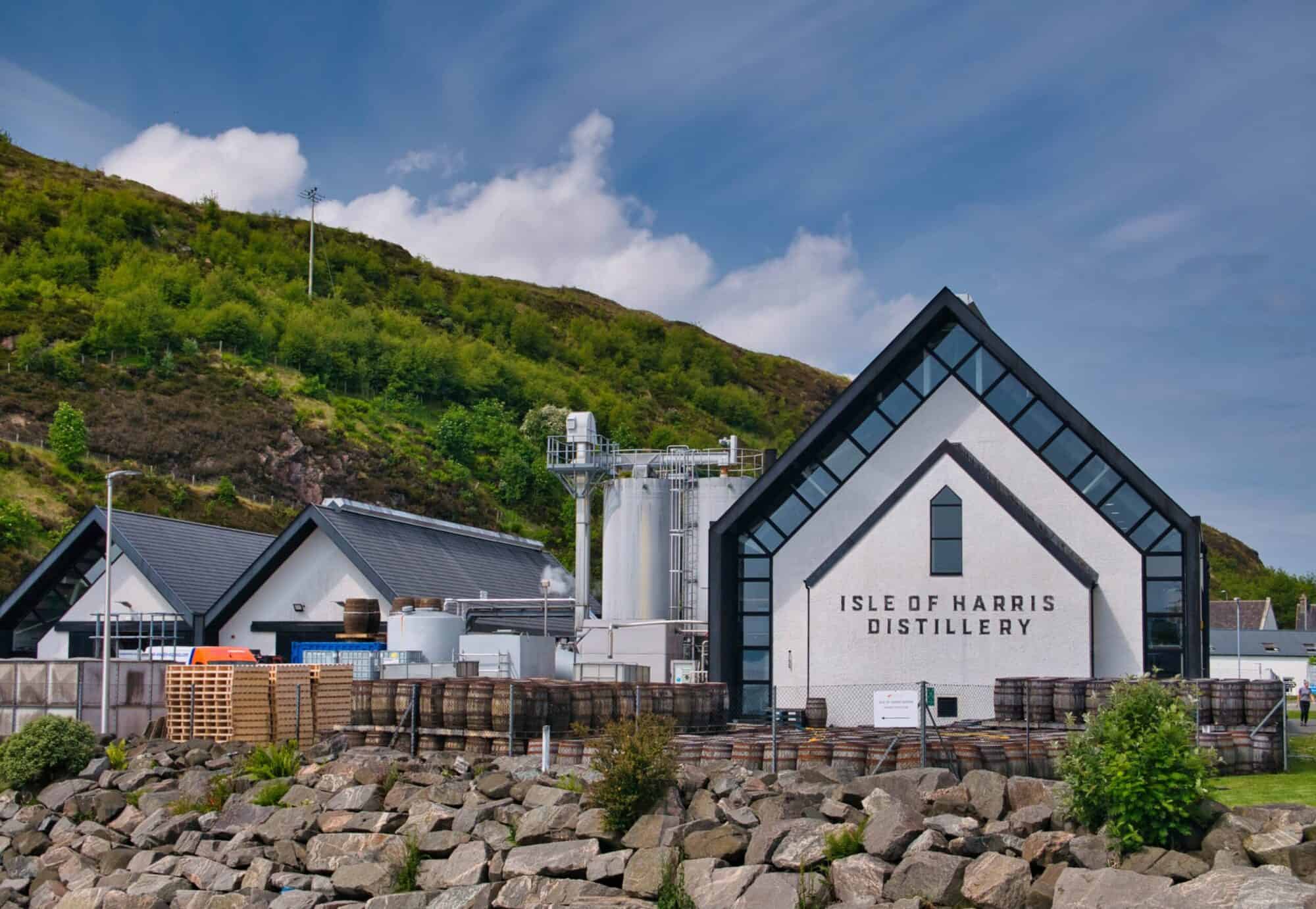 Modern distillery building at Isle of Harris Distillery with lush green hills in background.