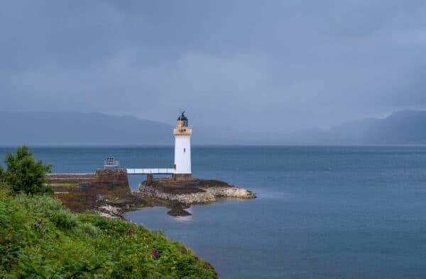 Lighthouse on rugged Scottish coast with lush greenery and ocean, perfect for Hebridean adventures.