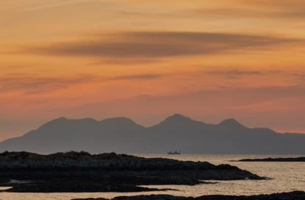 Bright sunset over Hebridean islands with mountains and calm sea, perfect for adventurous trips in the Scottish islands.
