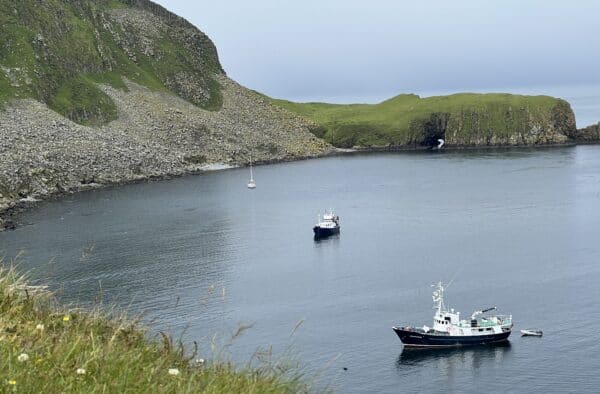 Serene harbour with boats & lush green cliffs, perfect for Hebridean adventures.