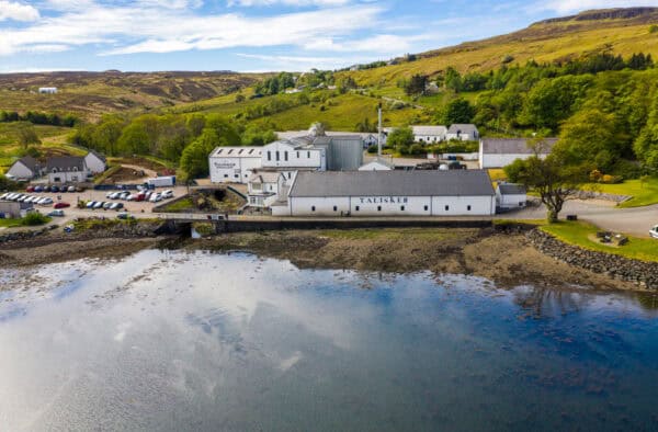 Talisker distillery on the Isle of Skye with scenic harbour and lush green hills in the background.