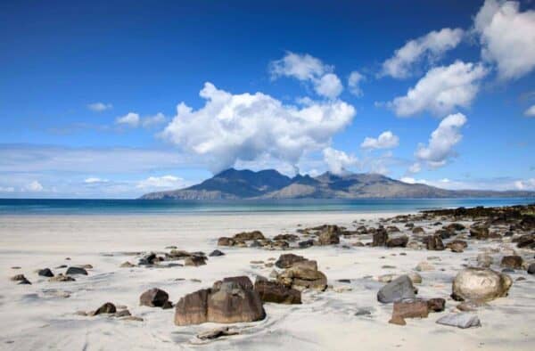 Beautiful Hebridean island beach with rocks and distant mountains under a bright blue sky.