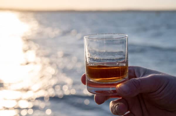 Close-up of a whisky glass held by a hand overlooking the ocean at sunset in the Hebrides.