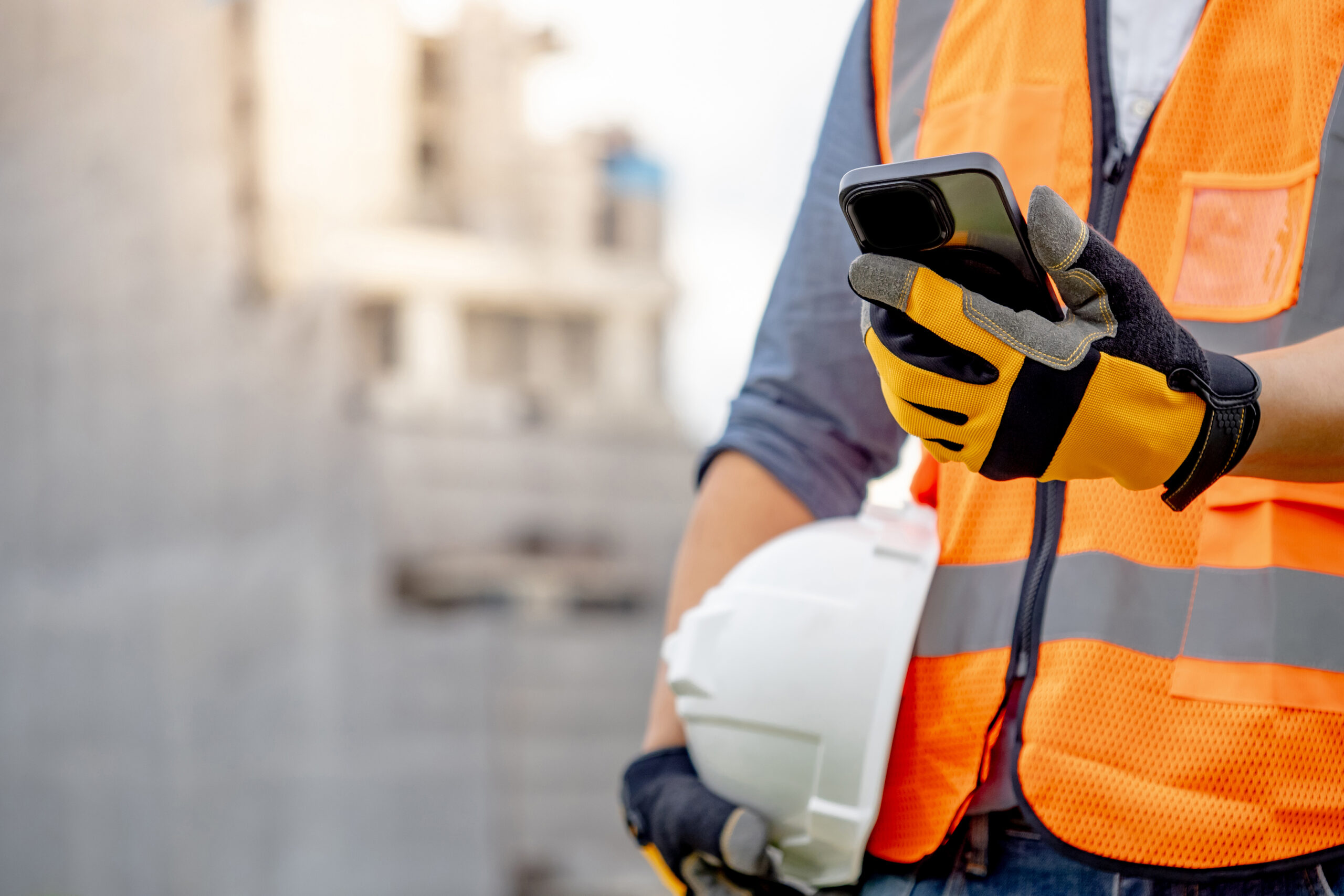 Gas services technician in safety gear checking smartphone at work site.