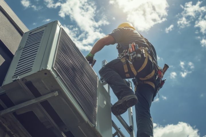 HVAC technician repairing air conditioning unit on building roof.