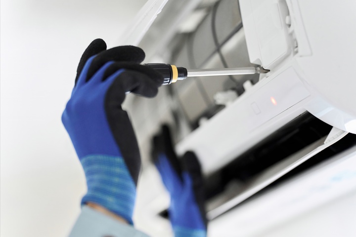 Gas technician repairing an air conditioning unit with a screwdriver.